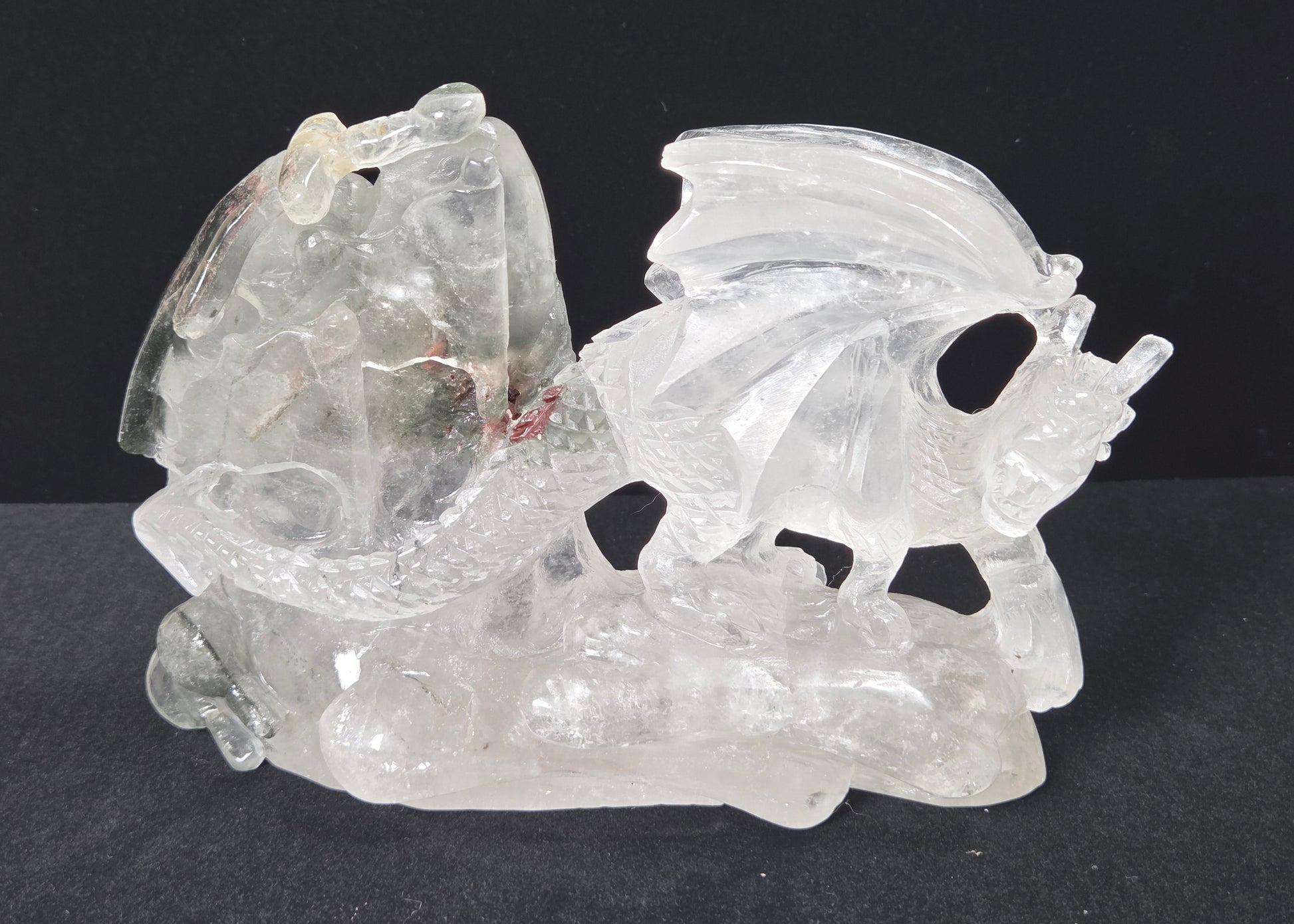 A carved clear crystal dragon figurine on a dark black background.