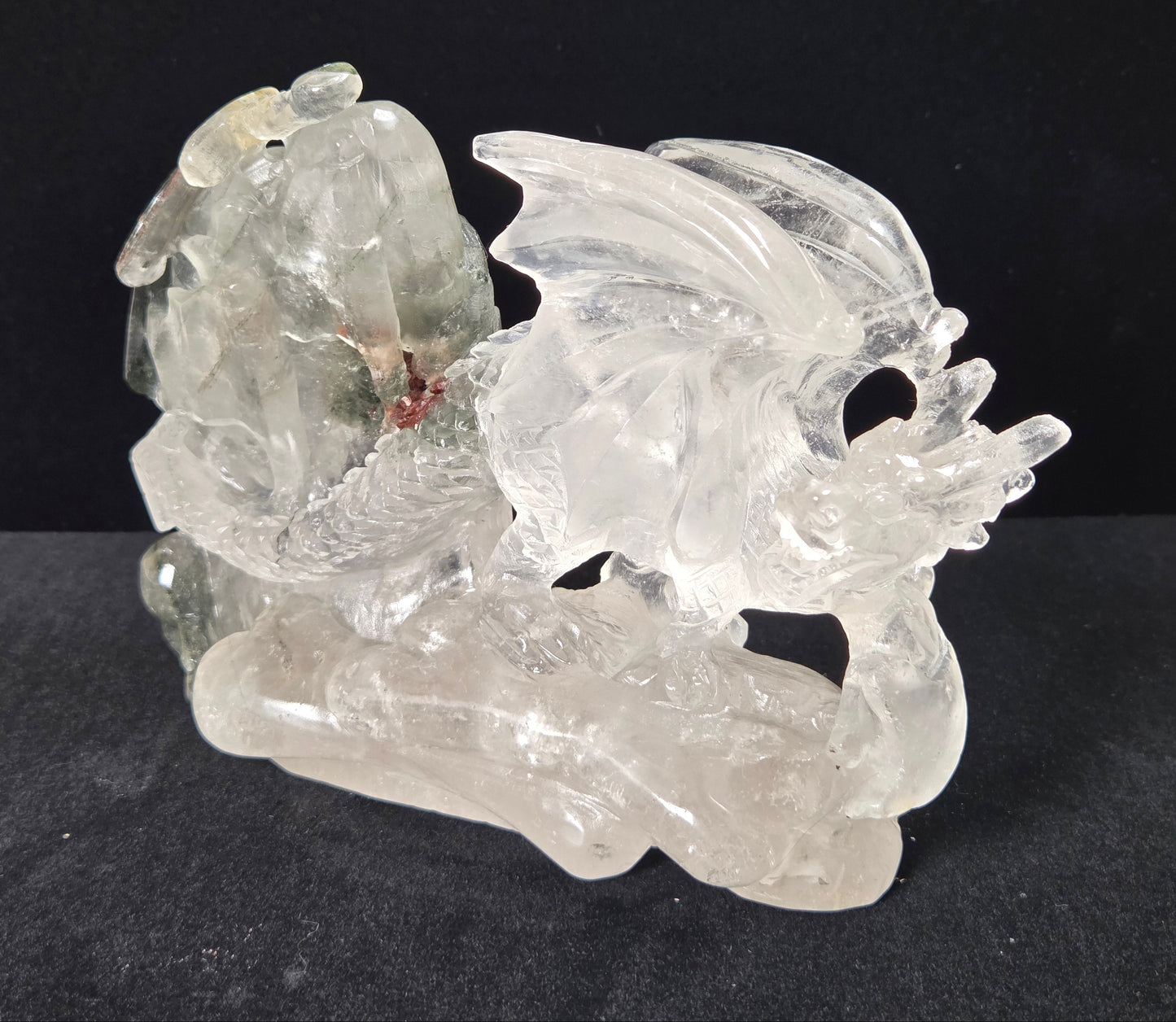 A carved clear crystal dragon figurine displayed on a dark textured surface against a solid black background.