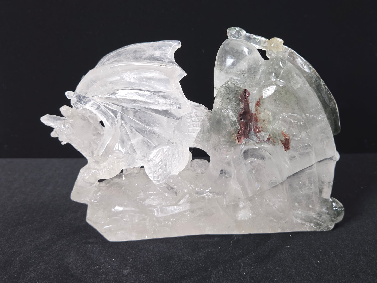 A clear, translucent carved stone sculpture depicting a winged figure on a base, photographed against a solid black background.