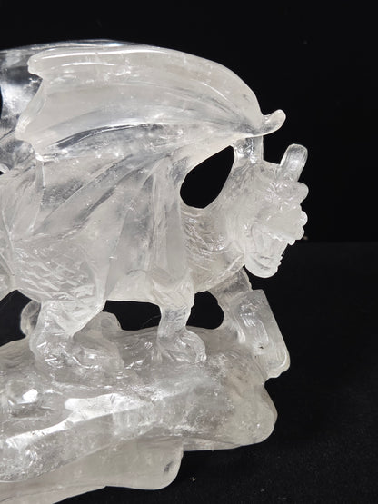 A clear crystal sculpture of a winged bull or ox standing on a rocky base, photographed against a solid black background.