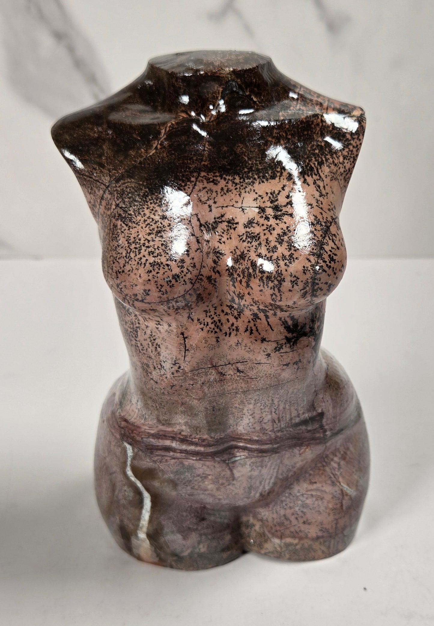 A small decorative torso sculpture with a glossy, mottled finish in dark brown, bronze, and gray tones, set against a light gray marble-patterned background.