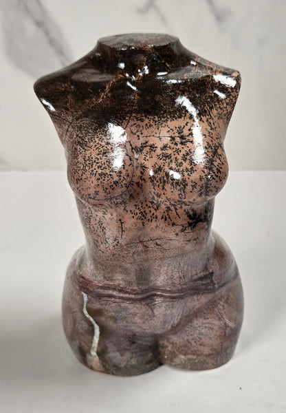 A small decorative torso sculpture with a glossy, mottled finish in dark brown, bronze, and gray tones, set against a light gray marble-patterned background.