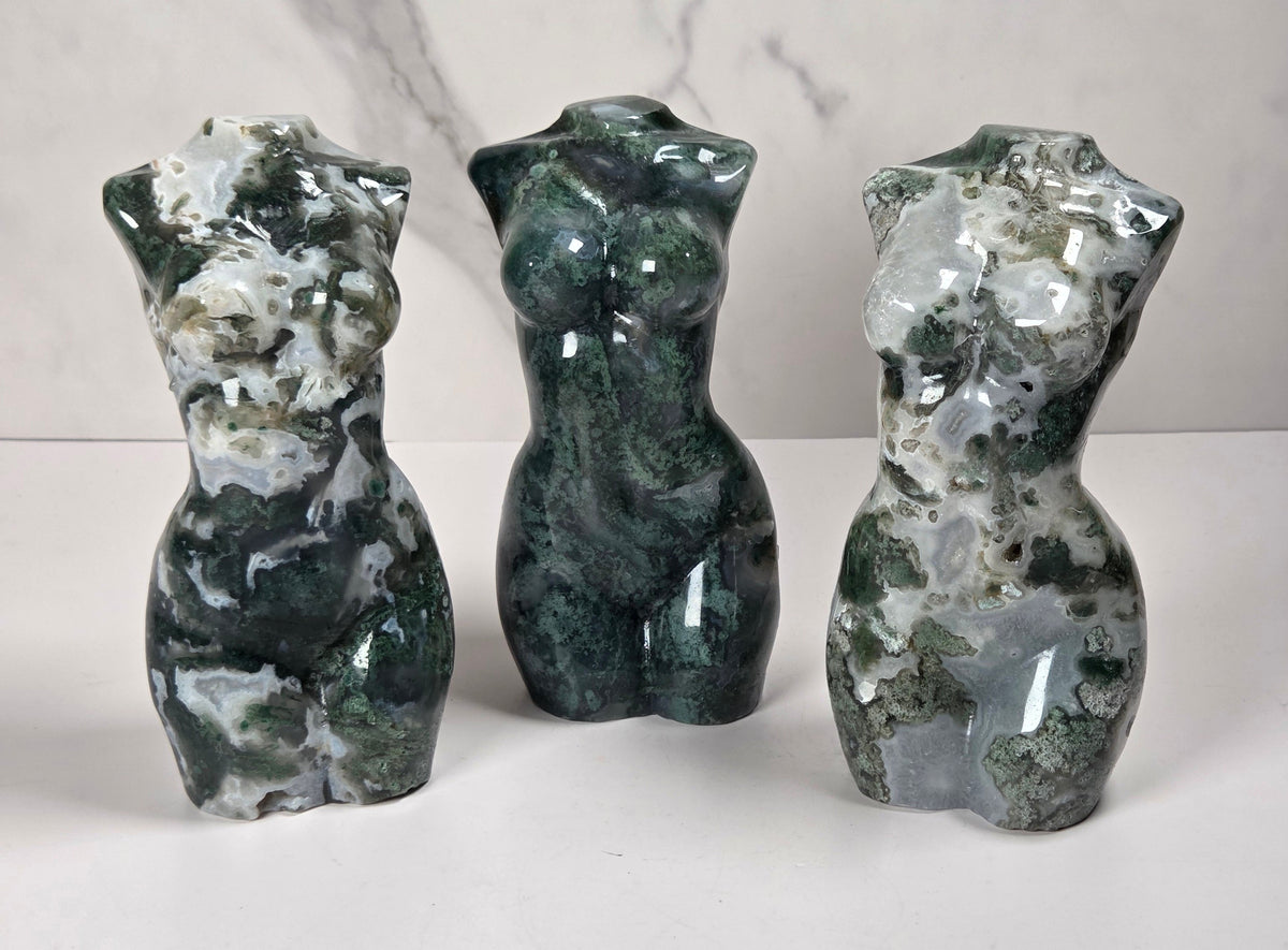 Three small sculptural torso figurines made from polished green and white marbled stone, displayed on a white surface against a light gray marble-patterned background.