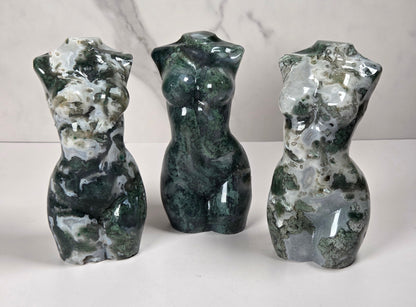 Three small sculptural torso figurines made from polished green and white marbled stone, displayed on a white surface against a light gray marble-patterned background.