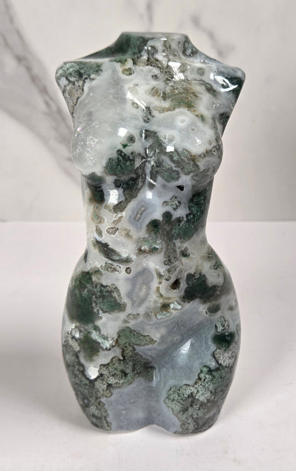 small sculptural torso figurines made from polished green and white marbled stone, displayed on a white surface against a light gray marble-patterned background.