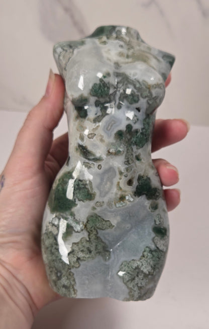  small sculptural torso figurines made from polished green and white marbled stone, displayed on a white surface against a light gray marble-patterned background.