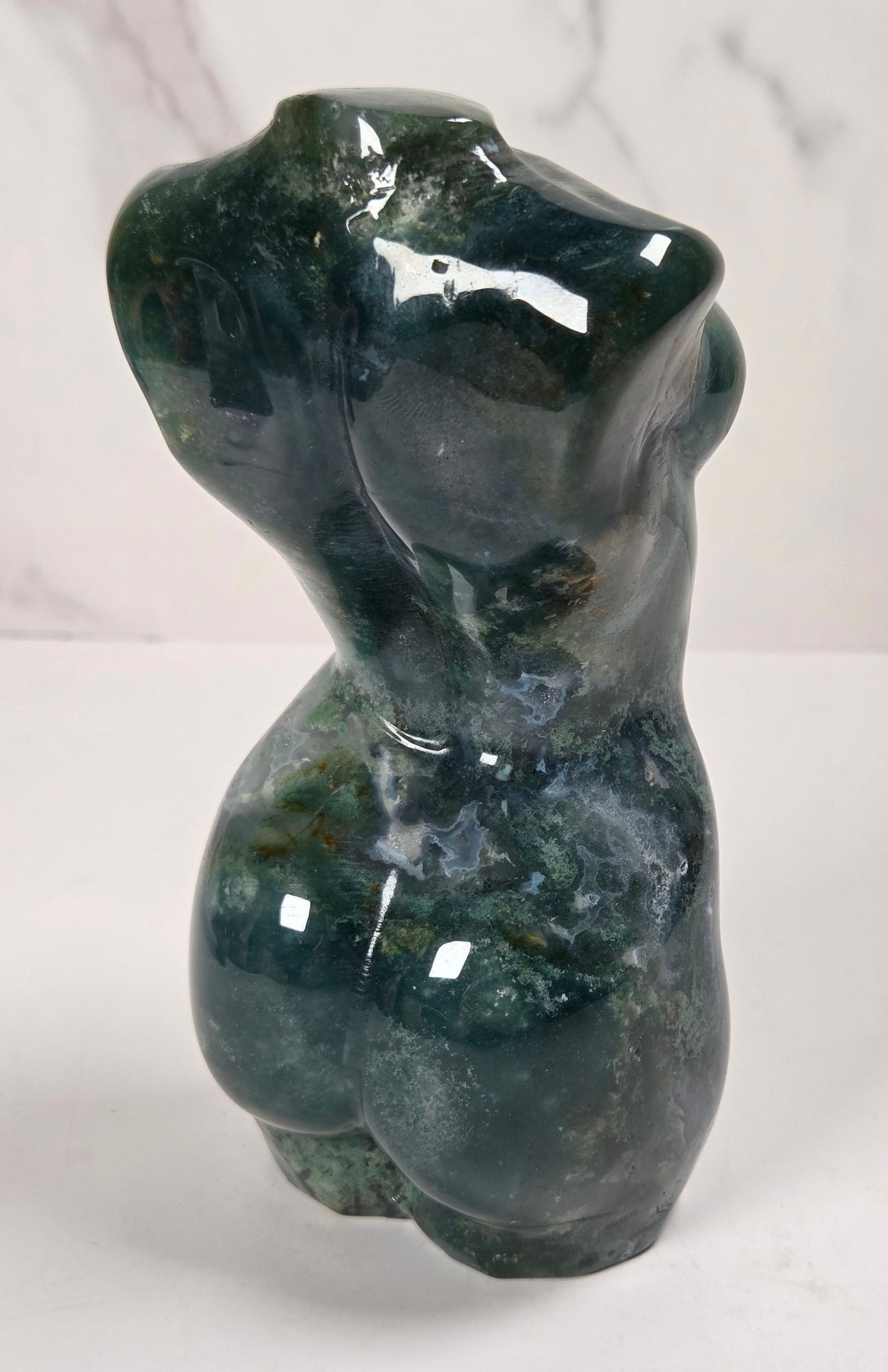  small sculptural torso figurines made from polished green and white marbled stone, displayed on a white surface against a light gray marble-patterned background.