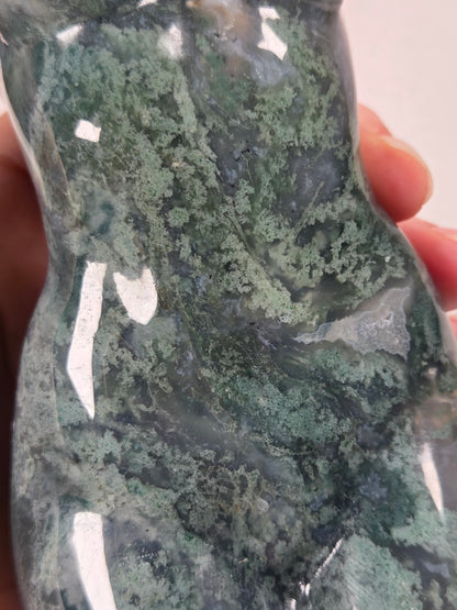 A close-up of a hand holding a polished stone or crystal with a marbled pattern of green, gray, and white tones.