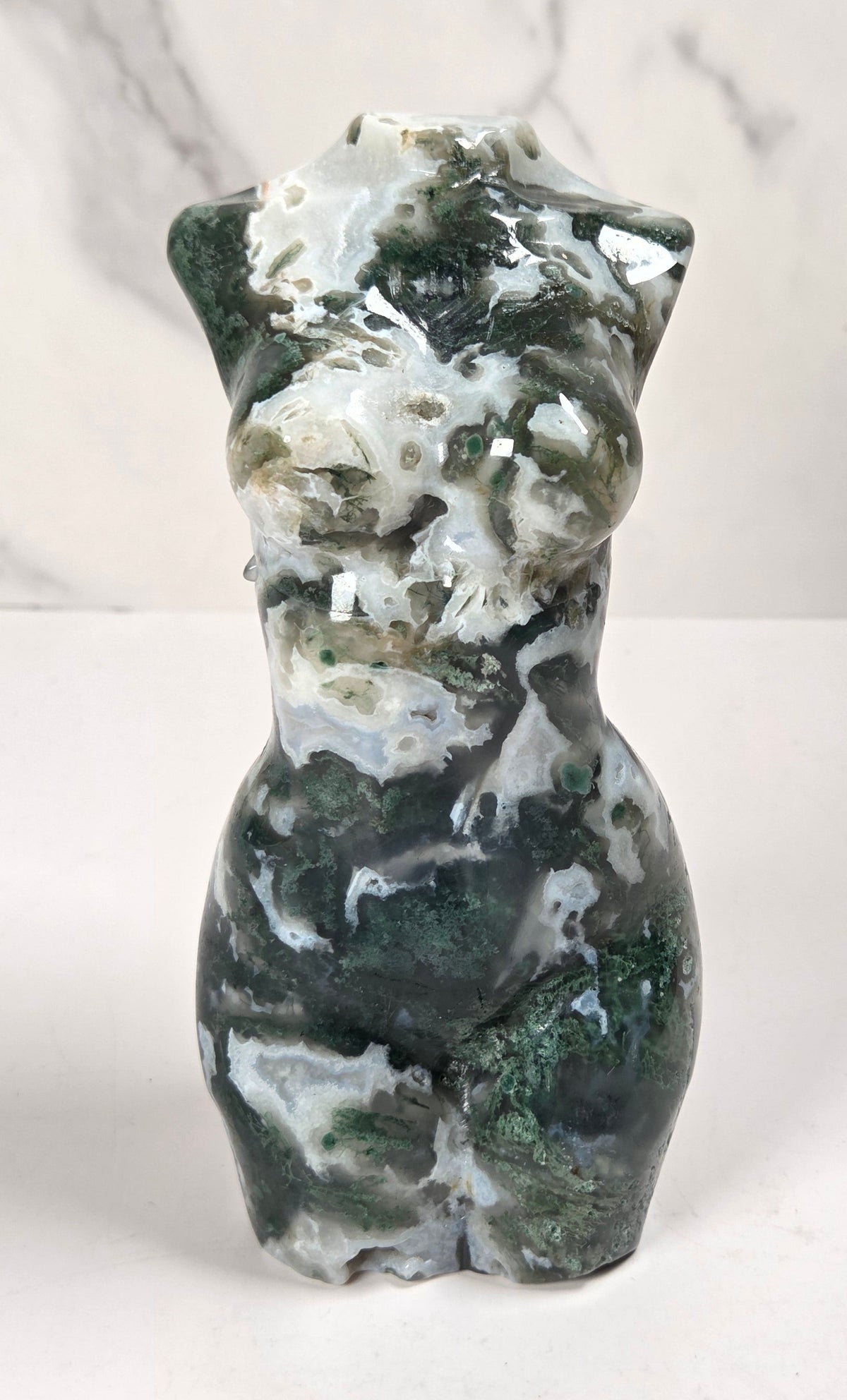  small sculptural torso figurines made from polished green and white marbled stone, displayed on a white surface against a light gray marble-patterned background.