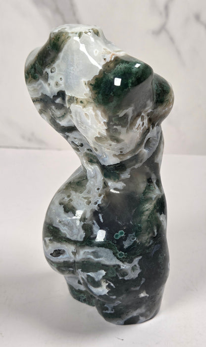  small sculptural torso figurines made from polished green and white marbled stone, displayed on a white surface against a light gray marble-patterned background.