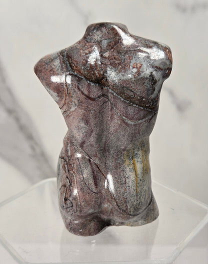 A polished decorative torso sculpture made from a marbled stone with brown, gray, and silver veining, displayed on a clear acrylic stand against a light gray marble-patterned background.