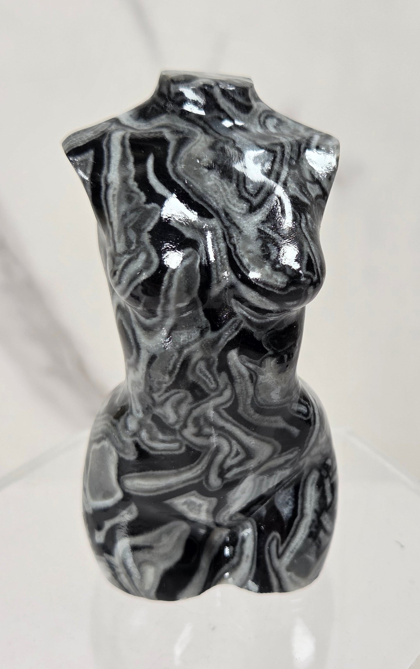 A glossy black and white marbled torso sculpture displayed on a clear acrylic stand against a light marble-patterned background.