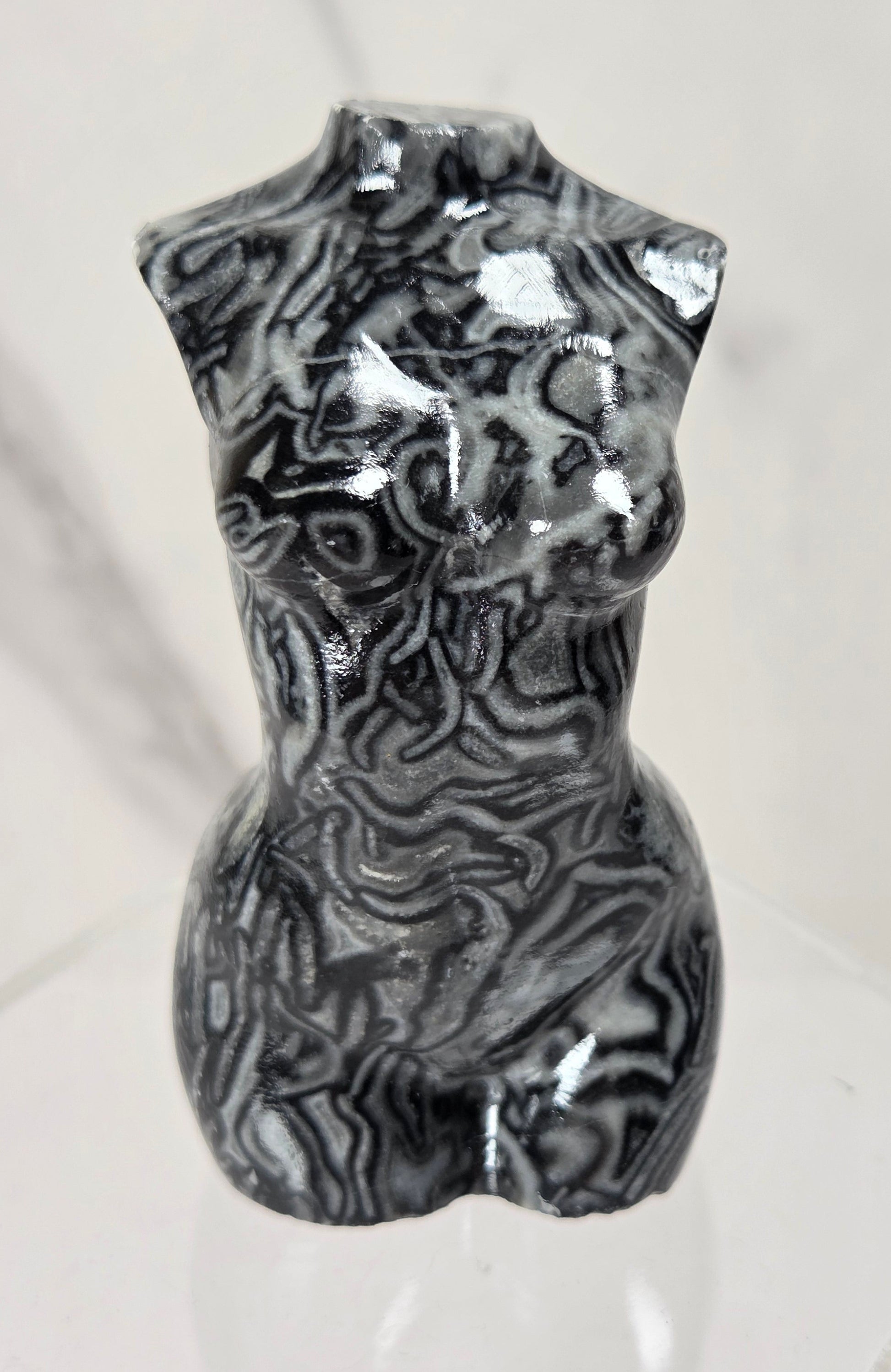 A glossy black and white marbled torso sculpture displayed on a clear acrylic stand against a light marble-patterned background.