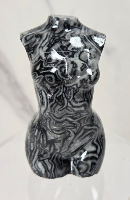 A glossy black and white marbled torso sculpture displayed on a clear acrylic stand against a light marble-patterned background.