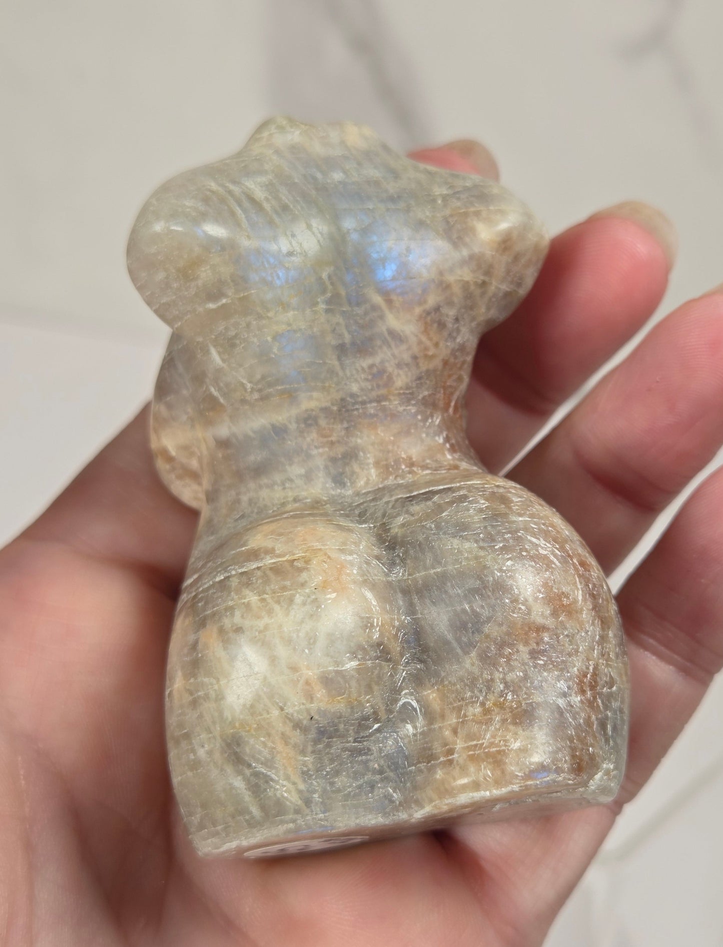 A hand holding a small, sculpted crystal figurine of a female form, showing natural labradorite iridescence.