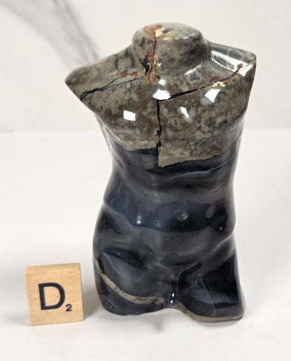 A small glossy ceramic torso sculpture with a split neck, shown on a white surface with a marble-look background. The upper half is mottled gray and black, and the lower half is dark navy blue.