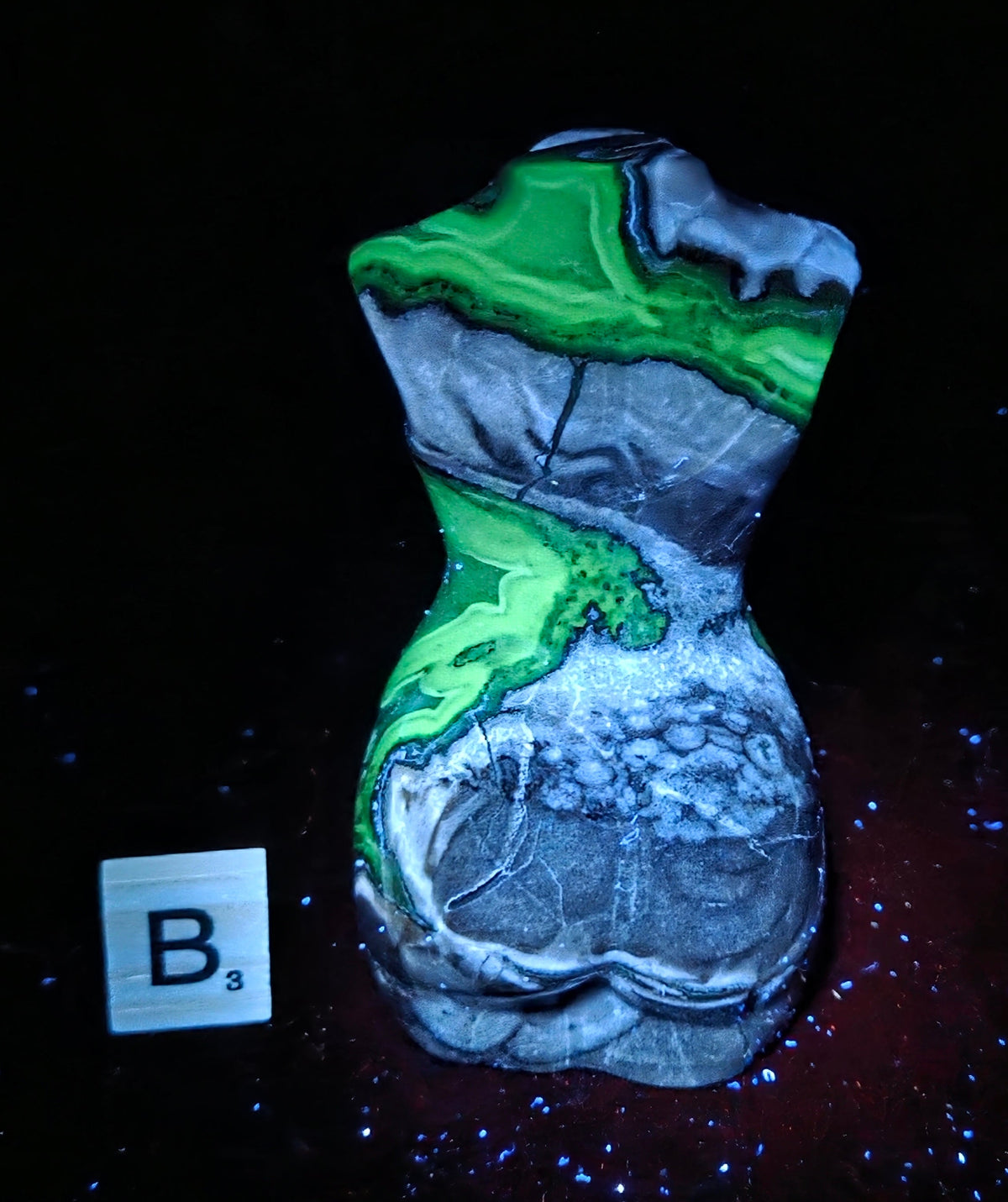 A torso-shaped decorative object with a marbled pattern of gray, white, and bright green, photographed against a black background with a small white square labeled B3 nearby.