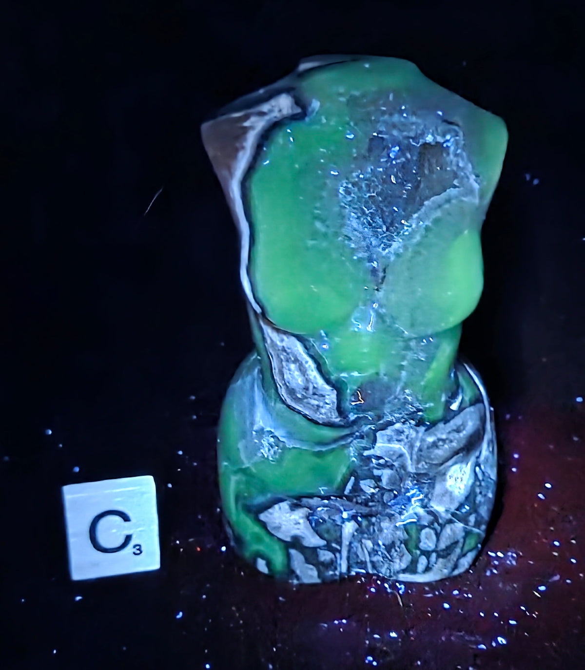 A sculptural bust or torso-shaped decorative object with a glowing neon green upper section and marbled gray, white, and black lower sections, photographed on a dark background with a small 'C5' card nearby.