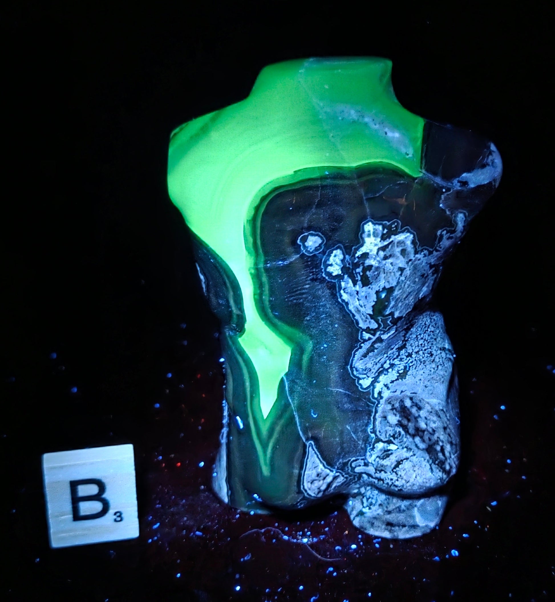 A glowing neon green and black decorative object with a marbled, stone-like texture, photographed on a black background with a small labeled card reading B3 nearby.