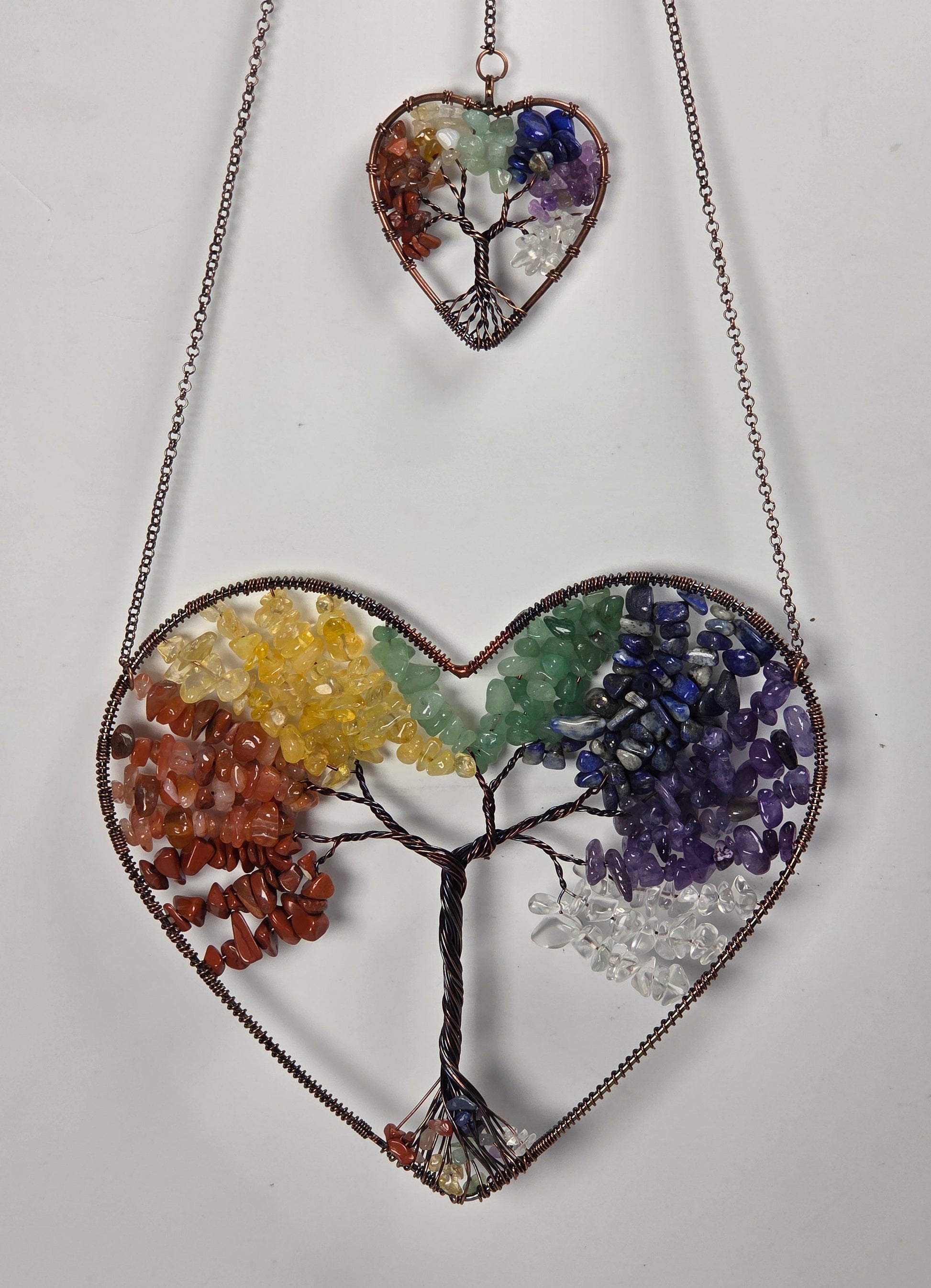 A heart-shaped chakra tree of life pendant necklace made of metallic wire and colorful gemstone chips, shown with its matching small heart-shaped pendant on a plain white background.