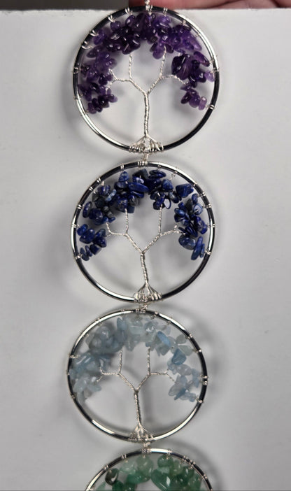 A vertical hanging wall ornament made of four circular silver frames, each containing a tree-of-life wire design filled with small gemstone chips in purple, blue, light blue, and green, shown against a plain white background.