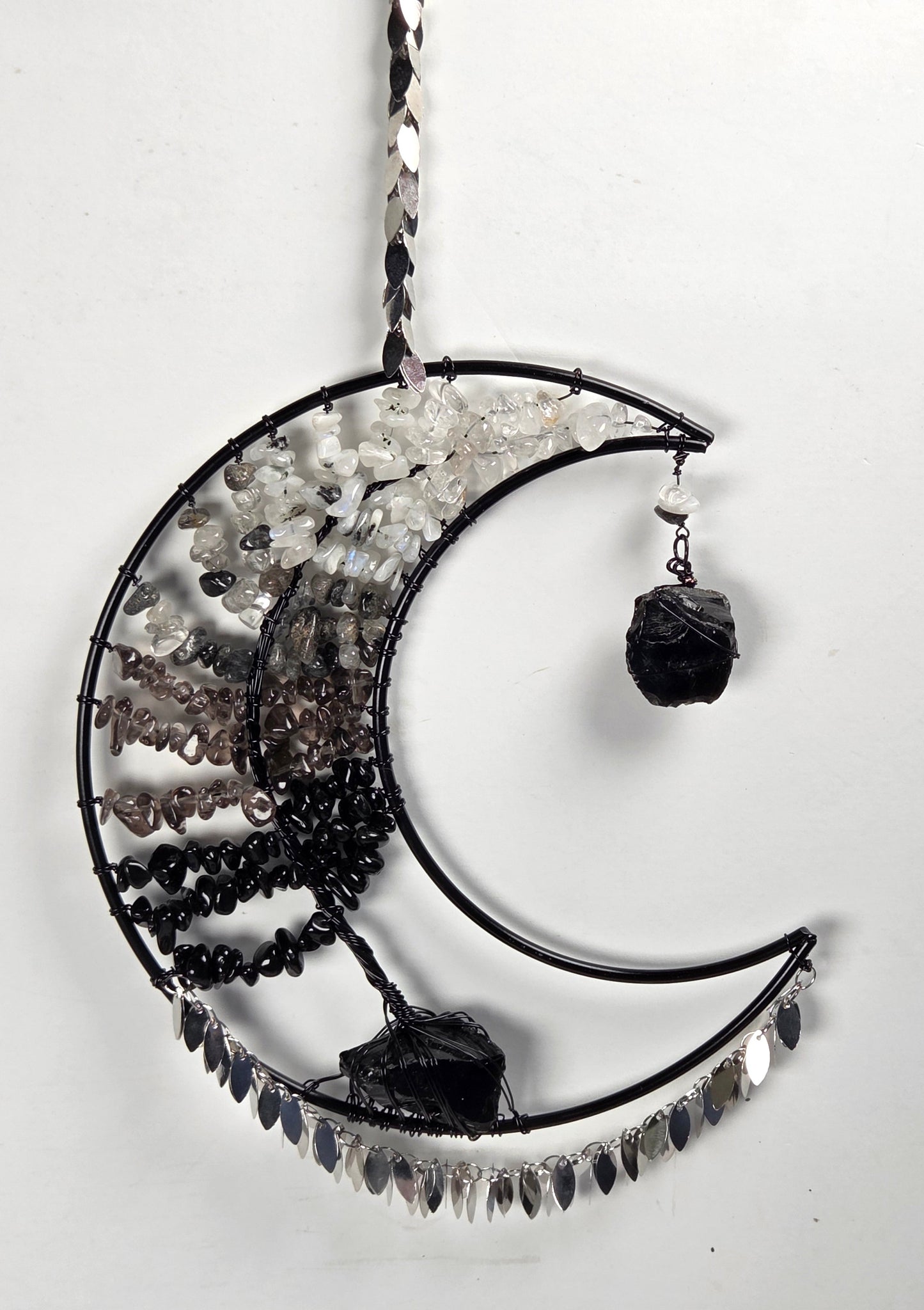 A crescent moon-shaped black metal hanging ornament decorated with clear quartz crystals, black beads, and dark smoky quartz stones, shown against a plain white background.
