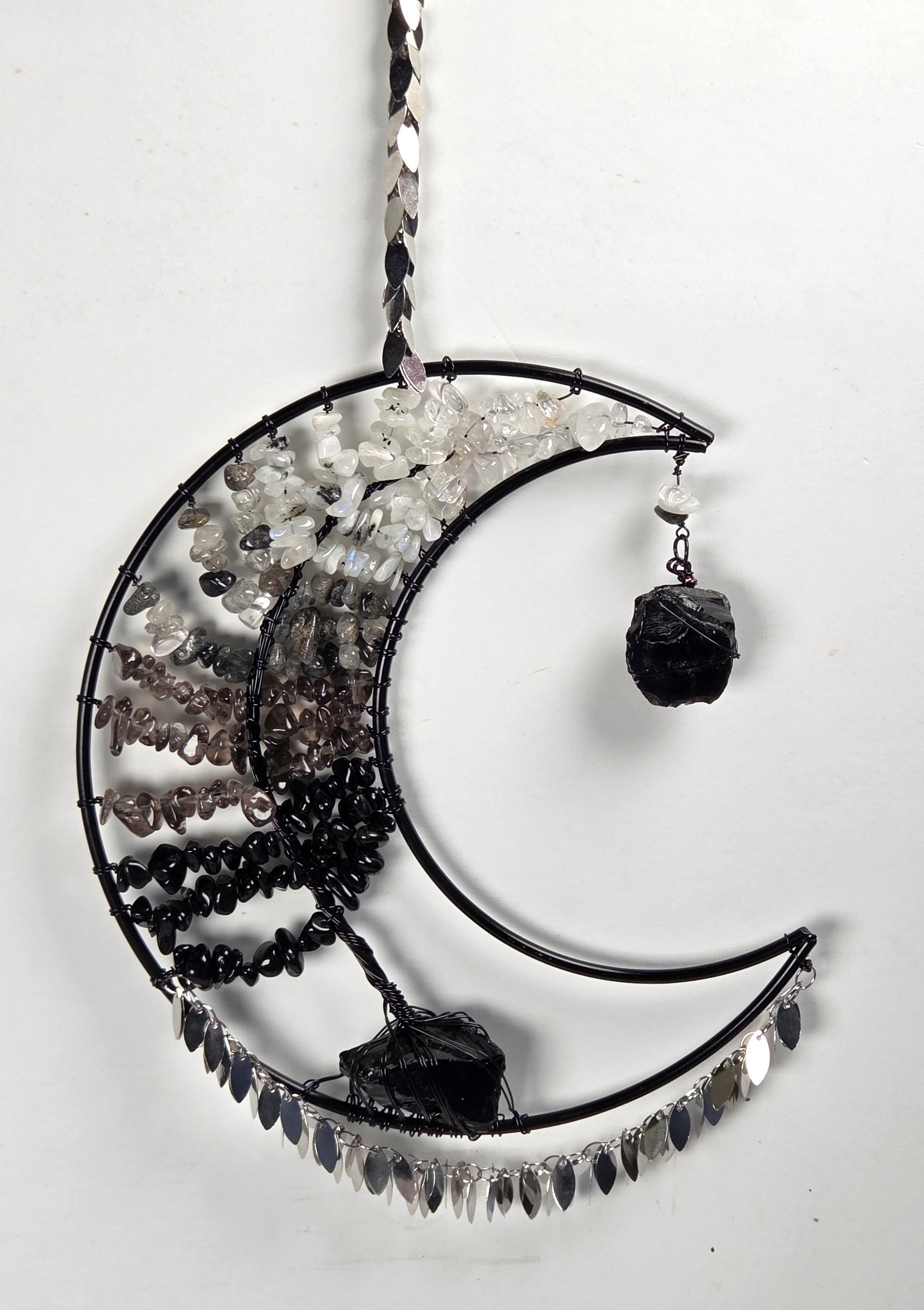 A crescent moon-shaped black metal hanging ornament decorated with clear quartz crystals, black beads, and dark smoky quartz stones, shown against a plain white background.