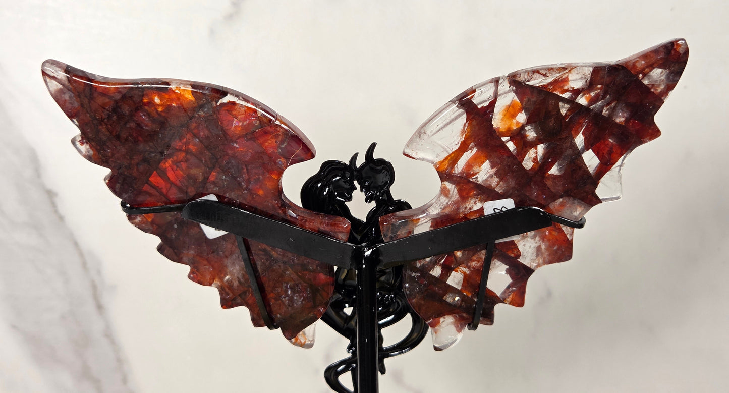 A decorative winged sculpture or ornament with two translucent reddish-brown wings and a black central figure and support, photographed against a light marble-like background.