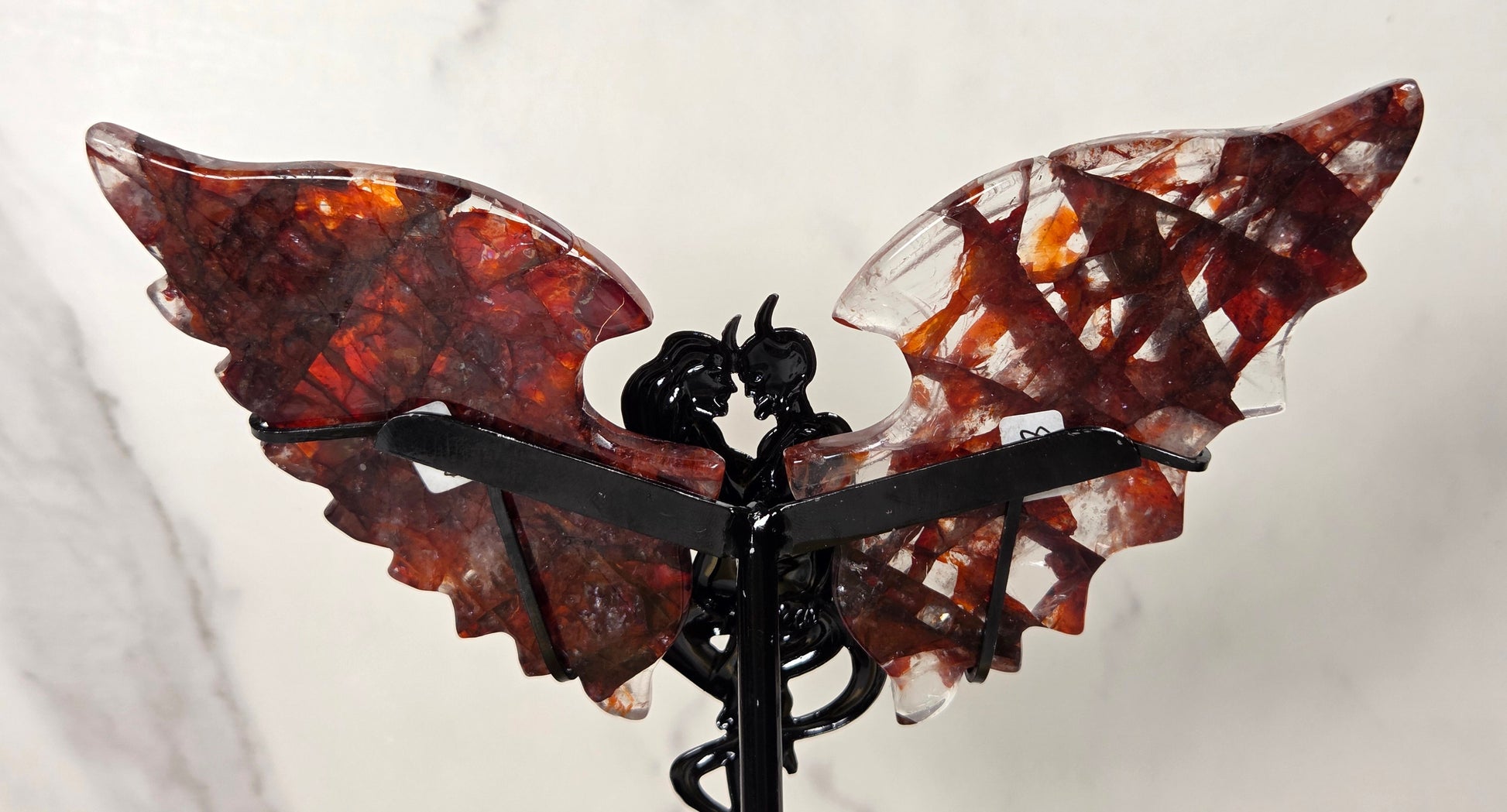 A decorative winged sculpture or ornament with two translucent reddish-brown wings and a black central figure and support, photographed against a light marble-like background.