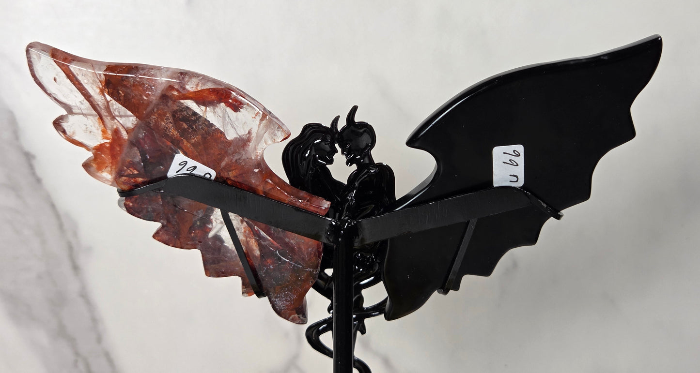 A decorative metal angel wing wind spinner featuring a glossy black bat-wing shaped metal frame and a translucent reddish-brown crystal wing, mounted on a black spiral stake against a light gray marble-patterned background.