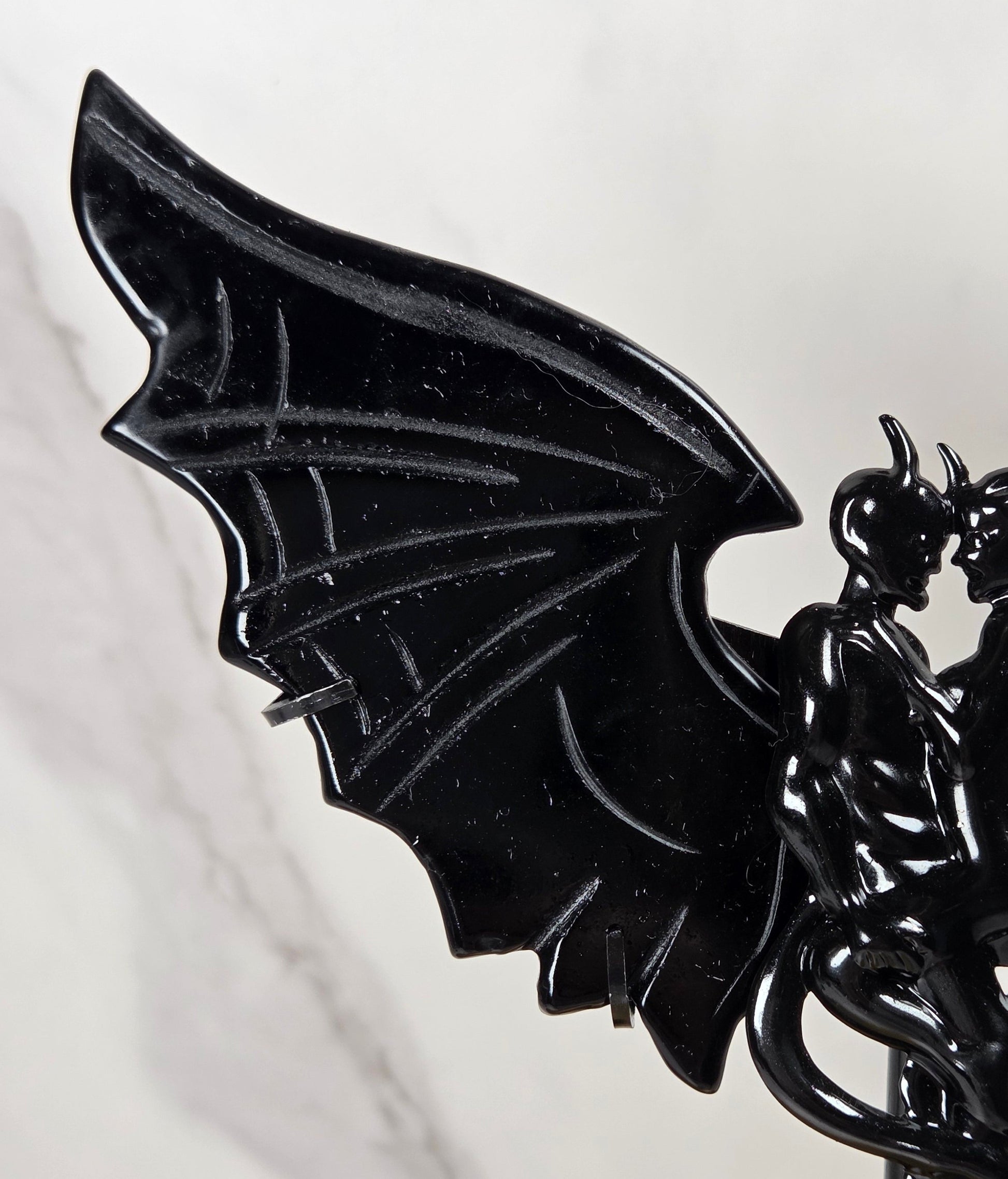A glossy black winged fantasy figurine or candle holder featuring a stylized dragon-like creature with spread wings and a coiled serpent detail, displayed on a stand against a light marble-patterned background.