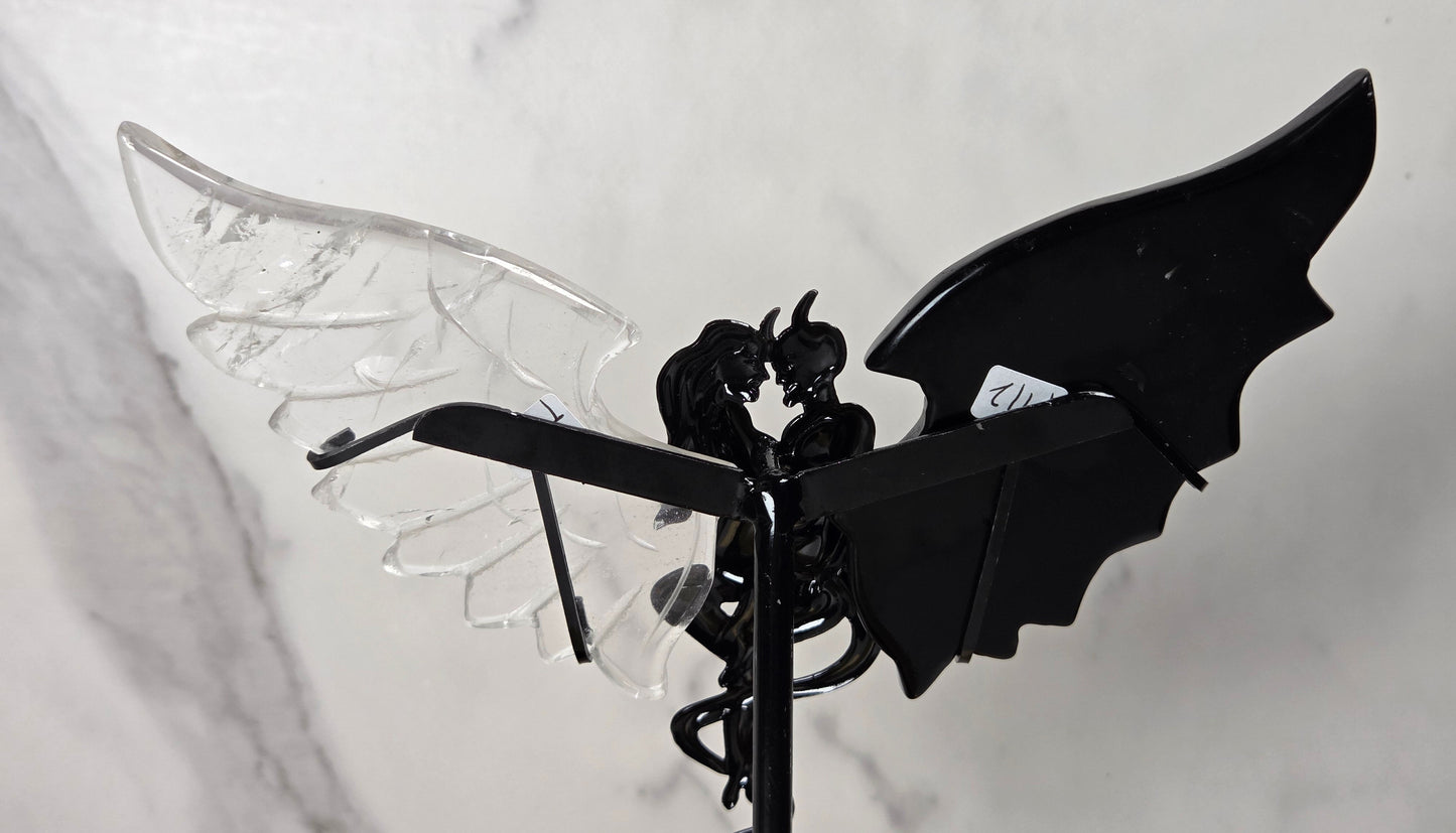 A gothic-style metal garden stake featuring a black winged figure with one transparent clear wing and one solid black wing, set against a light gray marble-patterned background.