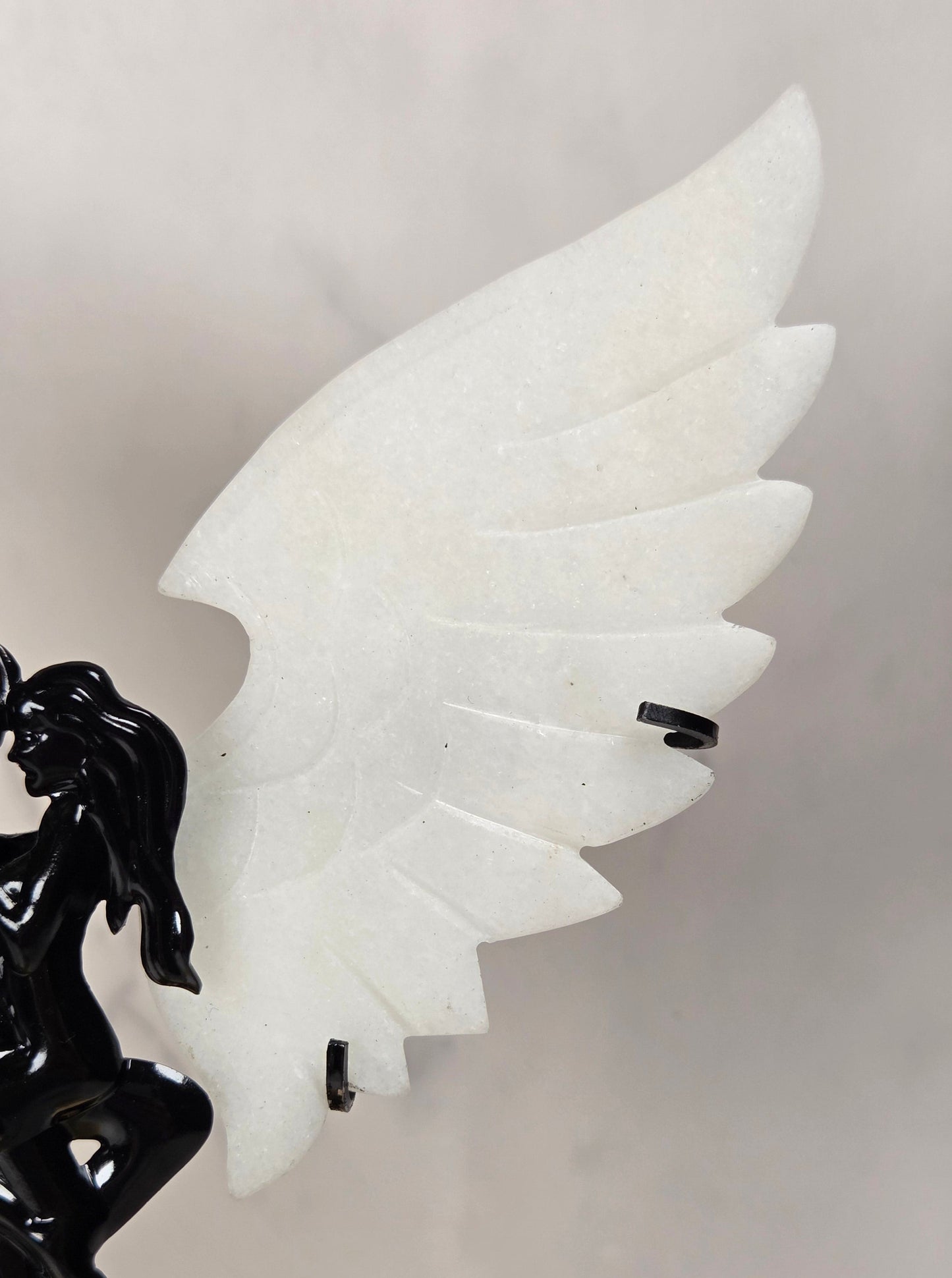 A close-up of a decorative sculpture featuring a glossy black winged figure on the left and a large white wing on the right, set against a soft light gray background.
