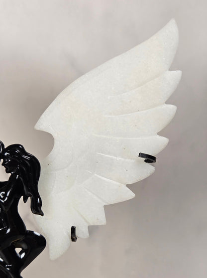 A close-up of a decorative sculpture featuring a glossy black winged figure on the left and a large white wing on the right, set against a soft light gray background.