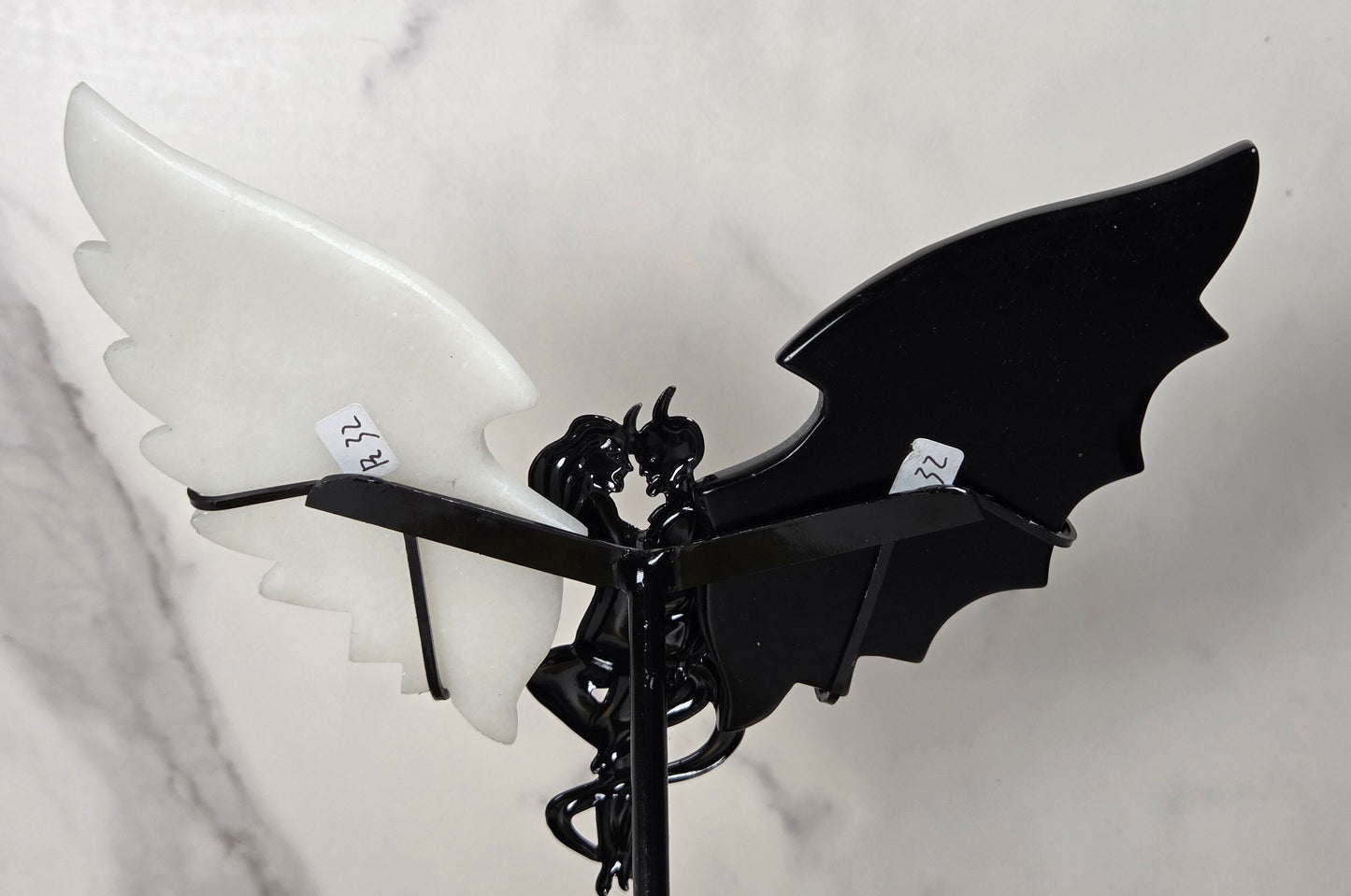 A decorative metal garden stake featuring a black bat-wing design with one glossy black wing and one matte white wing, mounted on a black spiral stake against a light marble-patterned background.