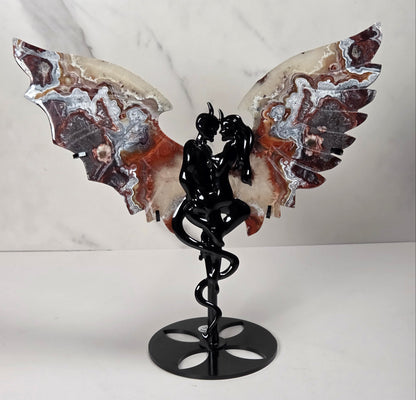 A winged female figure sculpture on a black metal staff base, set against a white marble-patterned background.