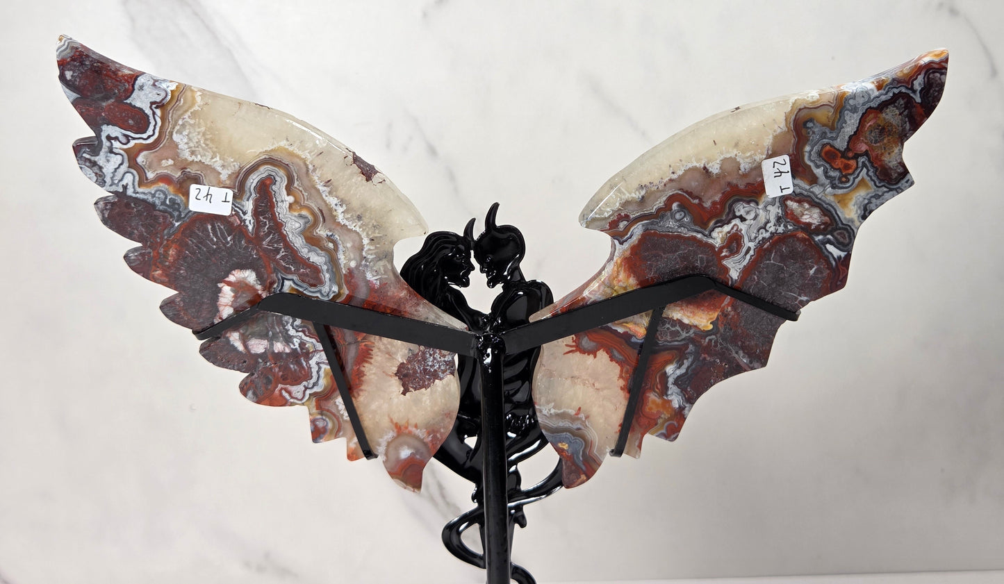 A decorative wing sculpture made from polished agate stone with swirling brown, cream, gray, and reddish patterns, mounted on a black metal stand against a white marble-patterned background.