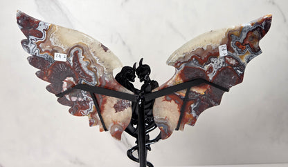 A decorative wing sculpture made from polished agate stone with swirling brown, cream, gray, and reddish patterns, mounted on a black metal stand against a white marble-patterned background.