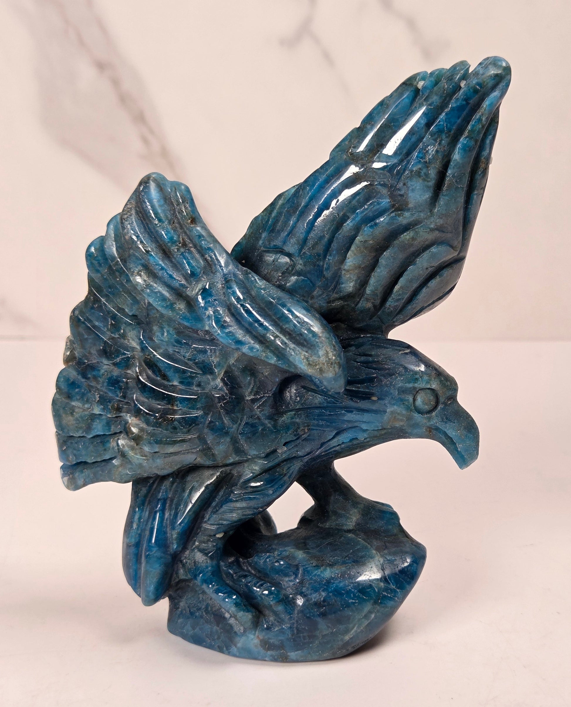 A blue stone eagle sculpture with wings spread, standing on a matching base, photographed against a light marble-patterned background.