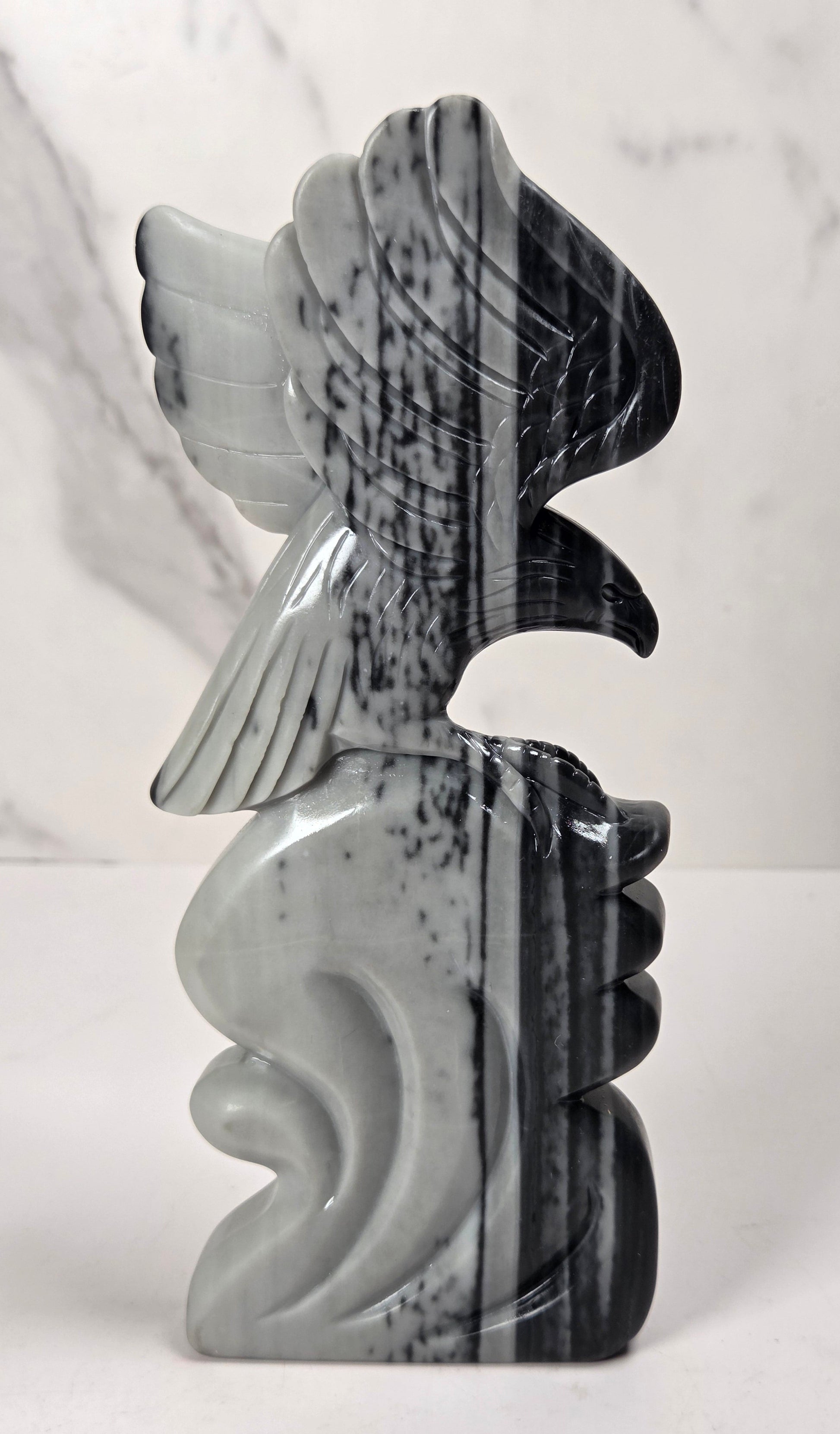 A sculpted decorative object with a stylized winged figure or abstract bird motif, made from polished black-and-white marbled stone, standing upright against a light marble-patterned background.