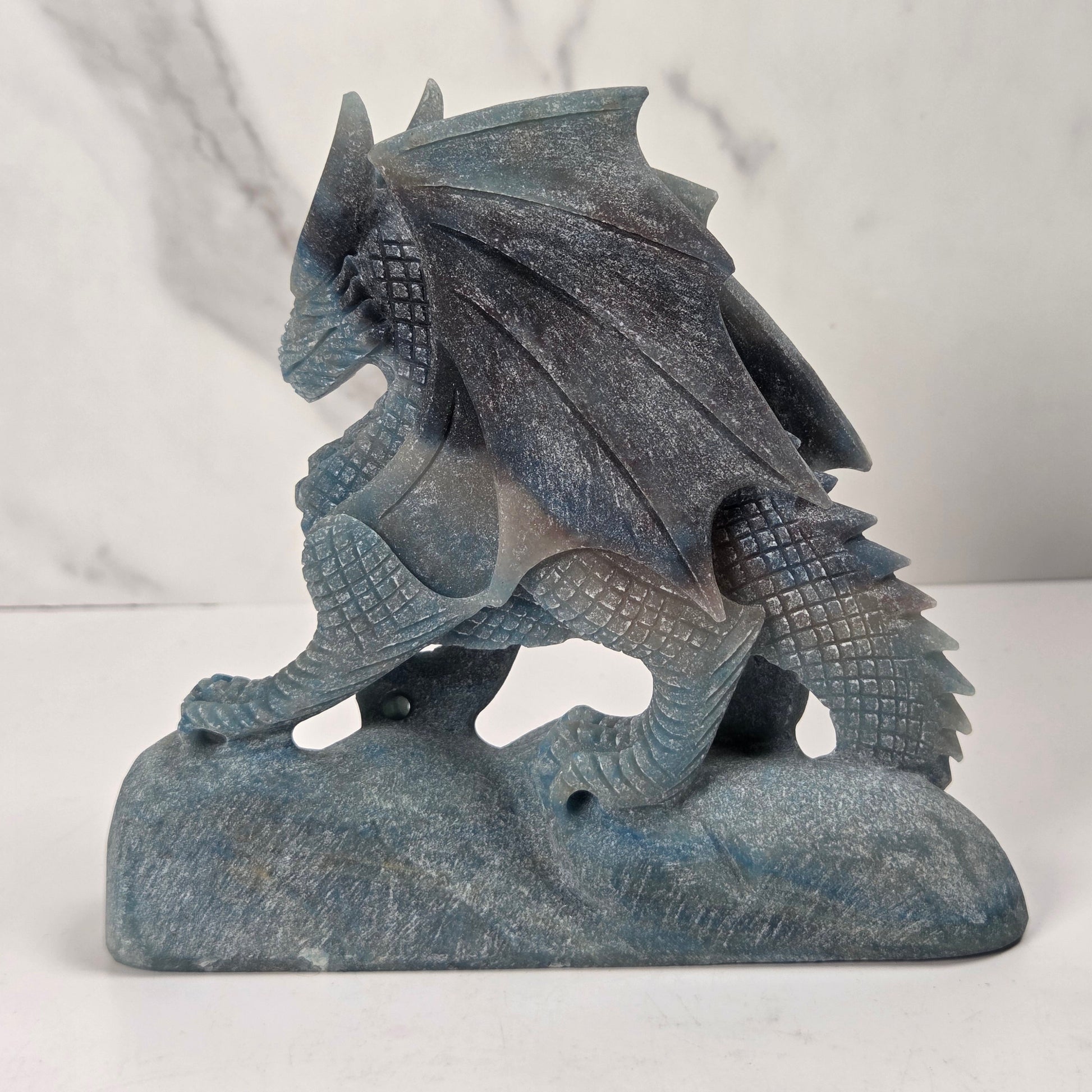 A blue-gray stone dragon figurine standing on a matching stone base, photographed against a light marble-patterned background.