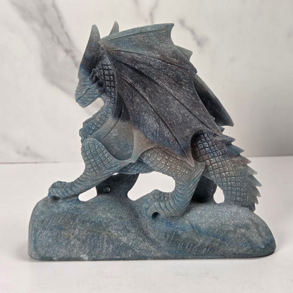 A blue-gray stone dragon figurine standing on a matching stone base, photographed against a light marble-patterned background.