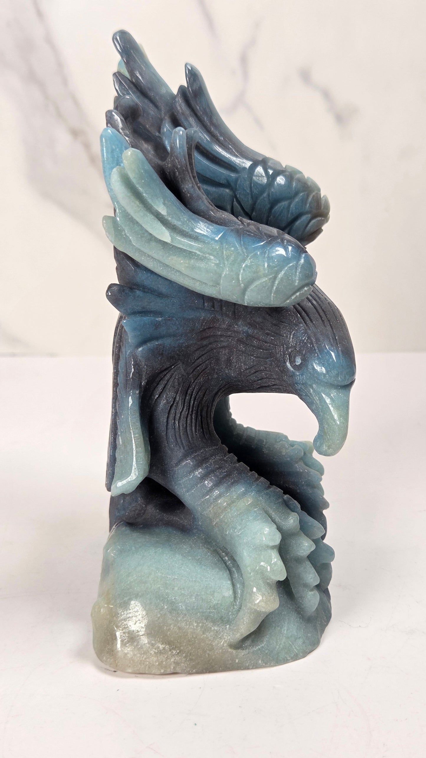 A carved stone sculpture of a bird of prey with wings spread, shown on a white surface against a light gray marble-patterned background.