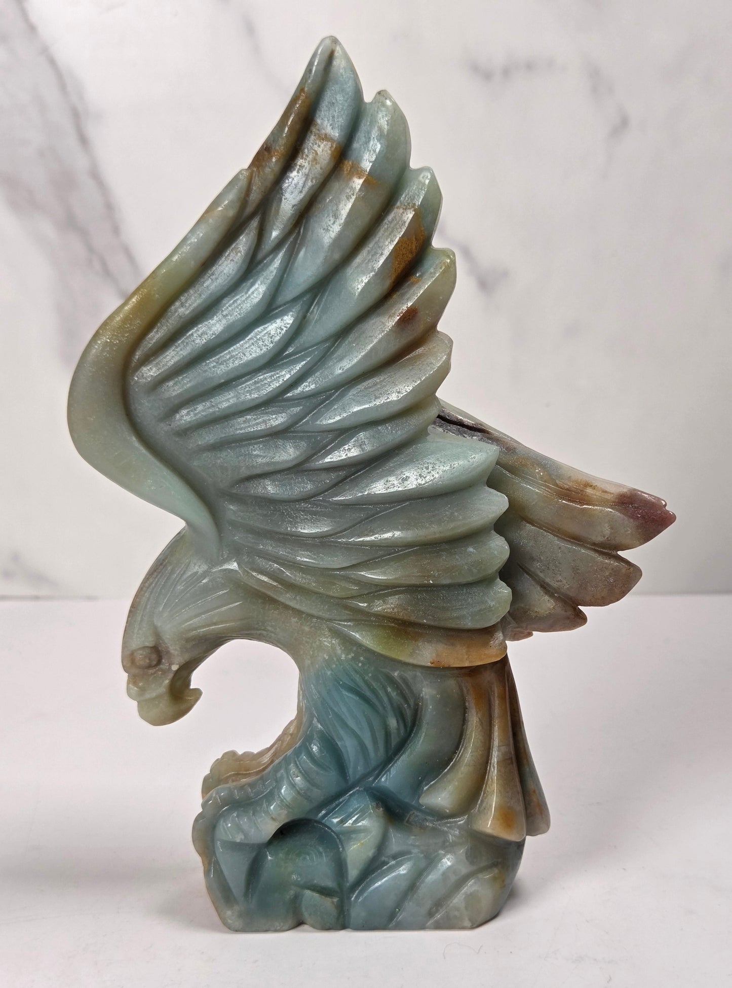 A carved stone eagle sculpture with wings spread, shown on a white surface against a light marble-patterned background.