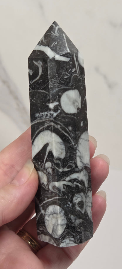 A hand holding a polished black and white marbled stone point tower against a light marble-patterned background.