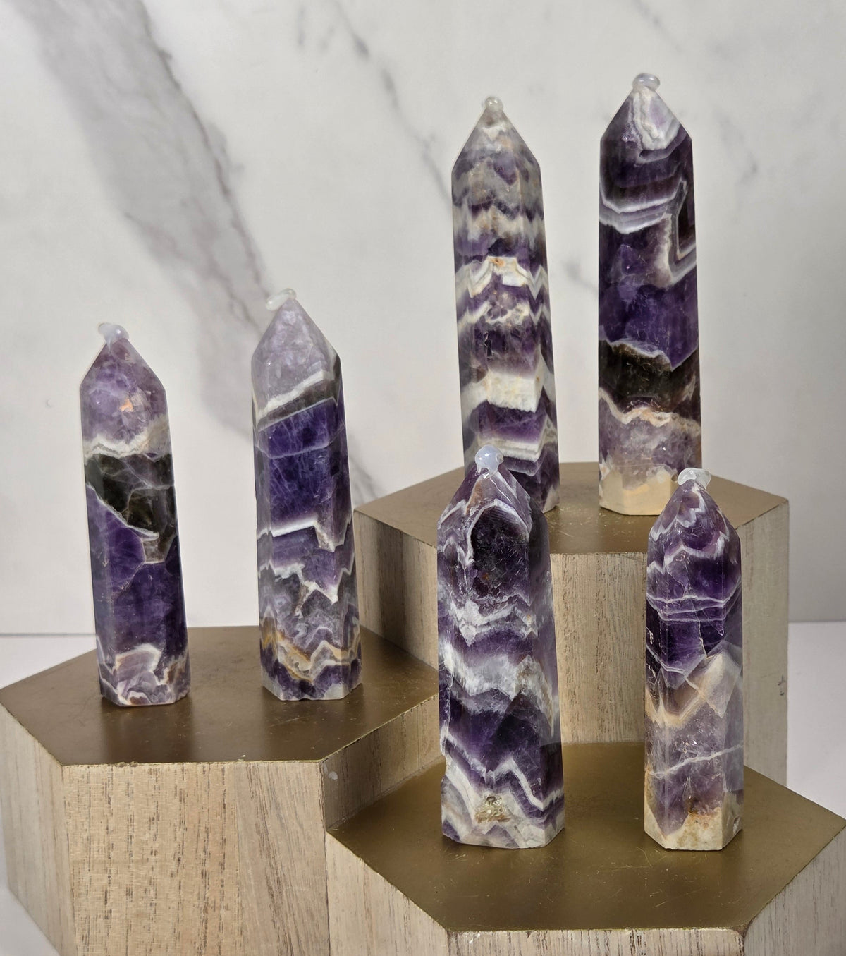 Five polished amethyst crystal points of varying heights, each resting on a hexagonal light wood block, arranged on a white surface against a white marble background.
