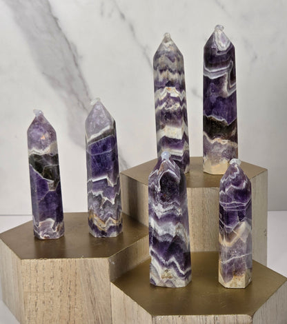 Five polished amethyst crystal points of varying heights, each resting on a hexagonal light wood block, arranged on a white surface against a white marble background.
