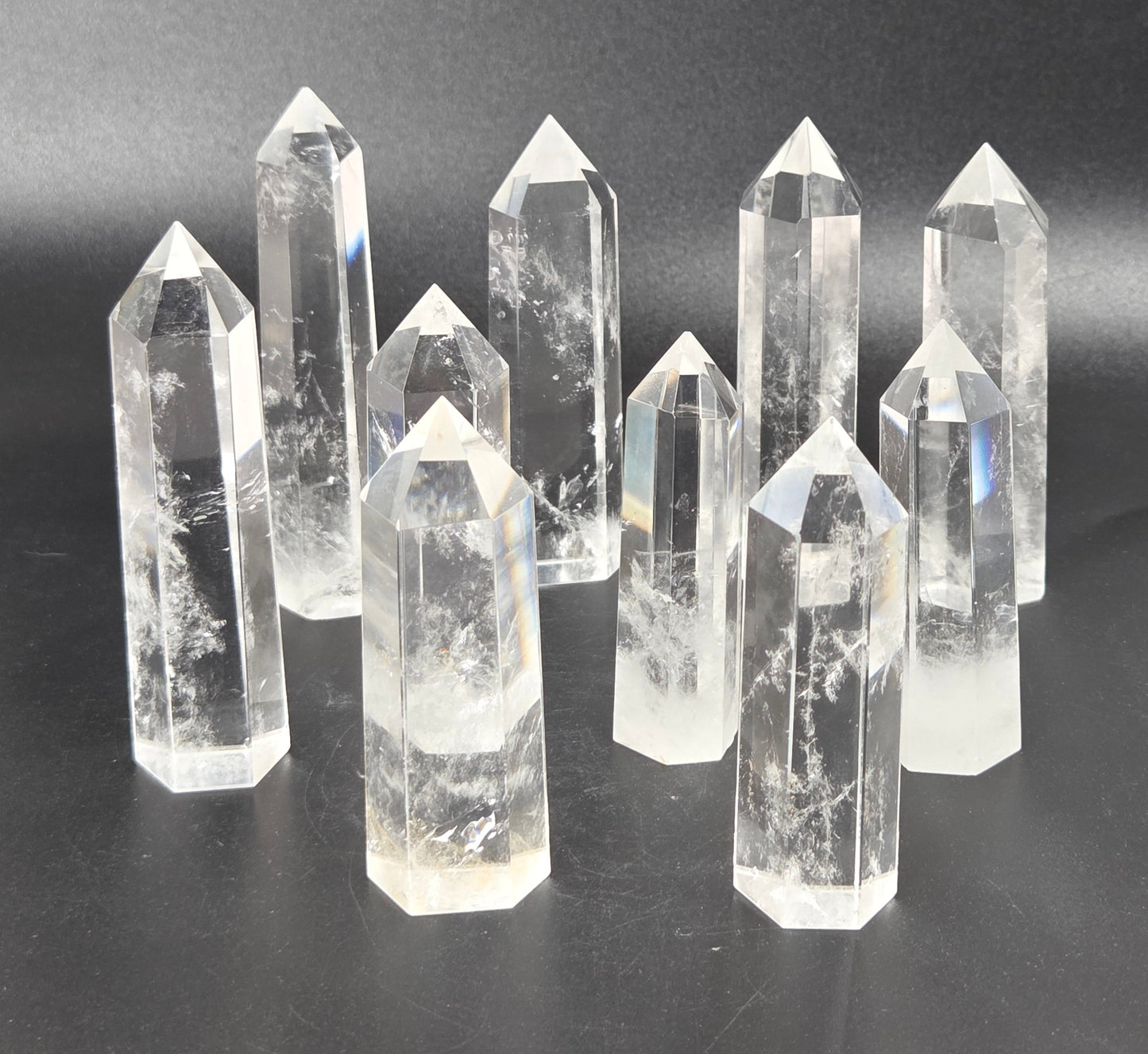 A set of clear quartz crystal points of varying heights arranged on a dark gray surface against a dark gray background.