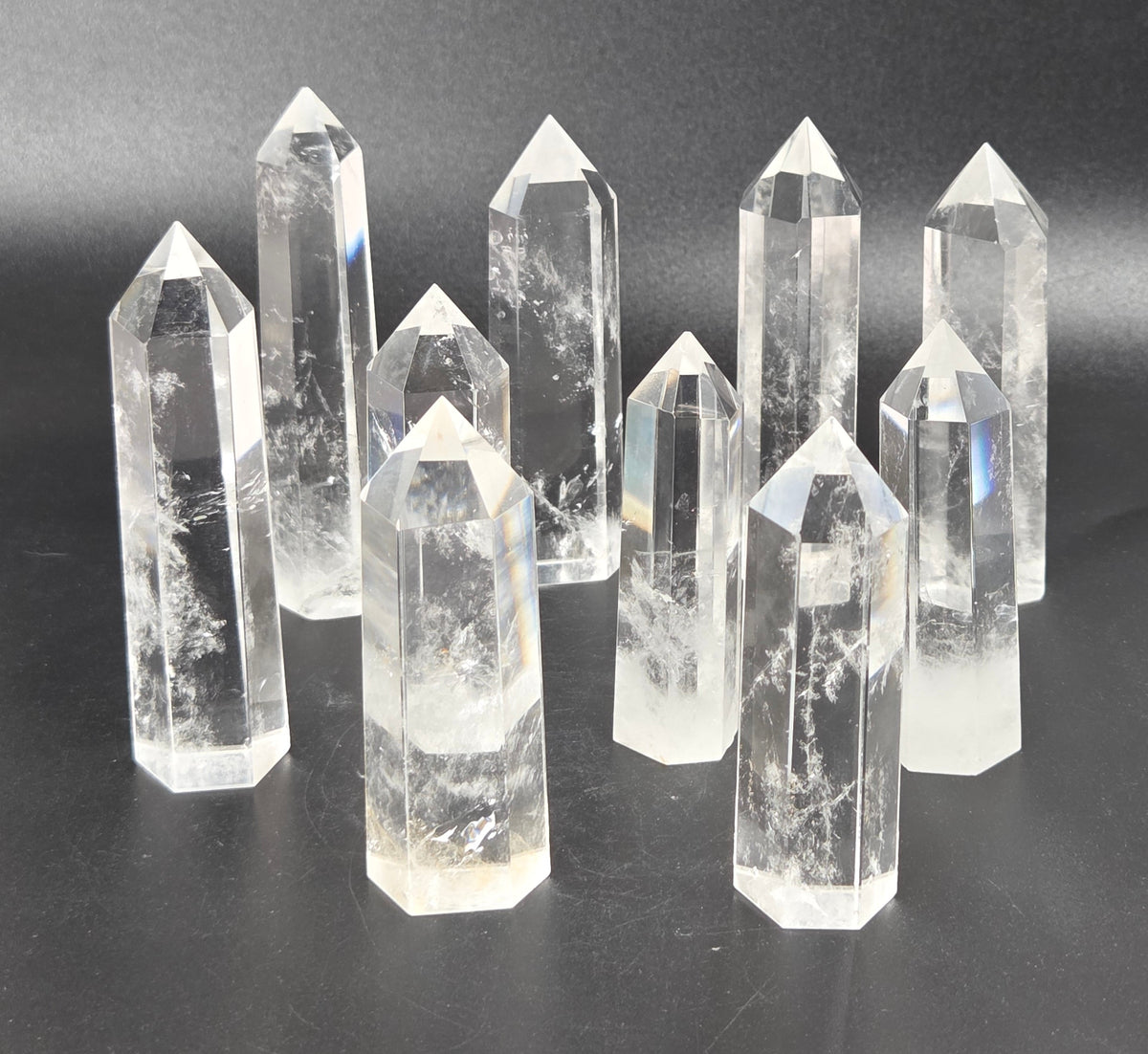 A set of clear quartz crystal points of varying heights arranged on a dark gray surface against a dark gray background.