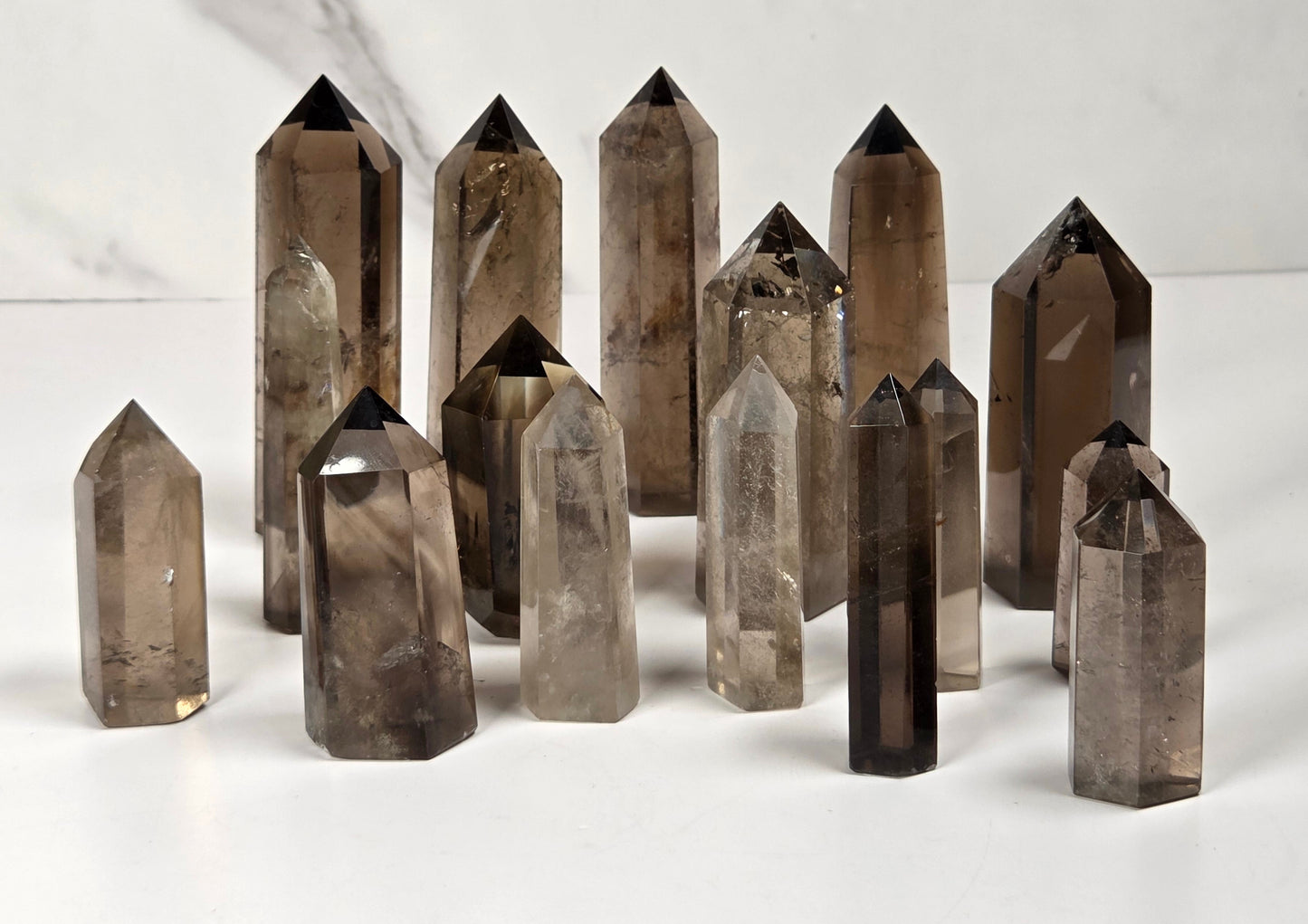 A group of smoky quartz crystal points of various sizes arranged on a white surface with a light gray marble-patterned background.